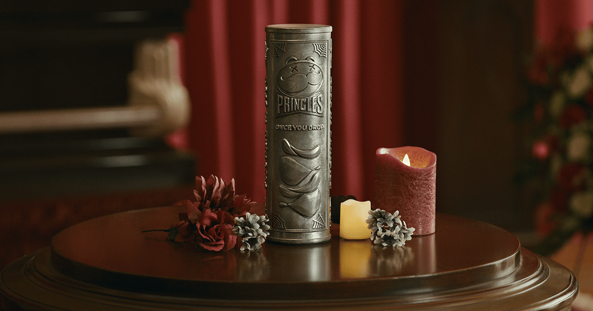 Une urne en métal gravé, de la forme exacte d’une boîte de Pringles, posée sur un guéridon entre des fleurs et des bougies