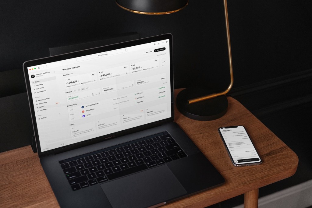Firma dashboard on a laptop beside a phone on a wooden desk