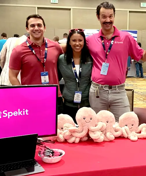 Three people standing behind a Spekit table with Speki mascot plushies.