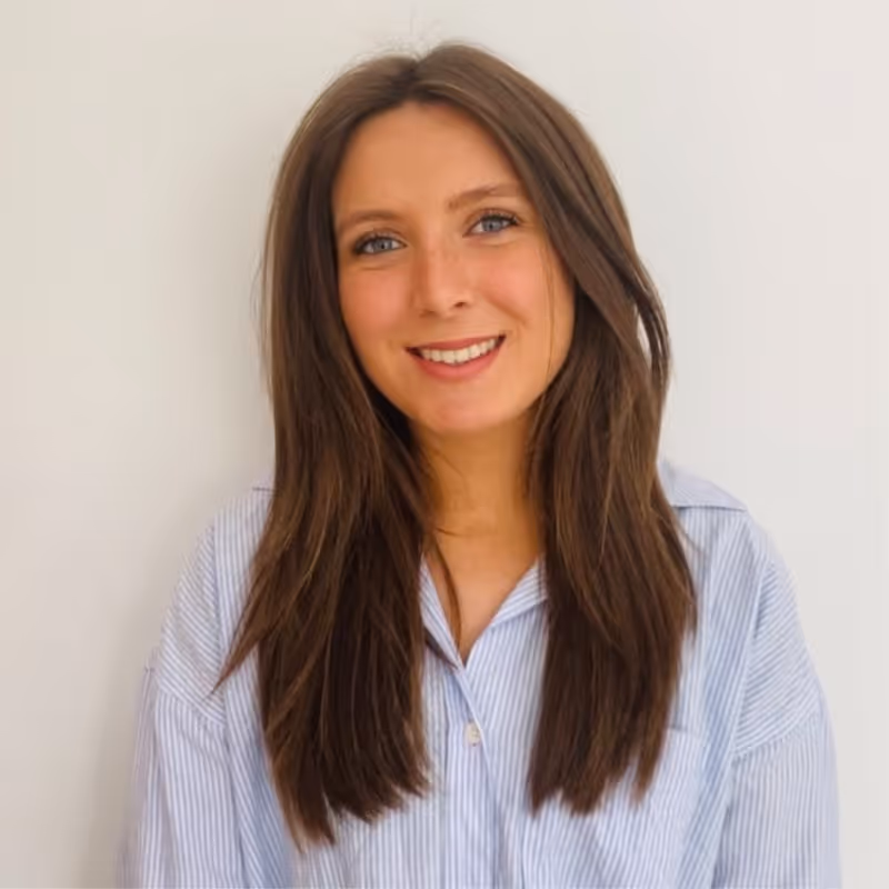Smiling woman with long brown hair wearing a light blue striped shirt against a plain white background.