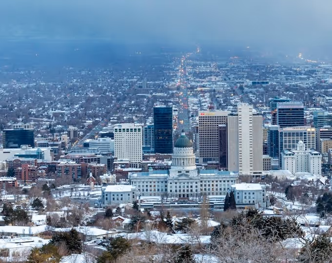 Snow-covered Salt Lake City skyline featuring the Utah State Capitol building with mountains obscured by fog in the background.