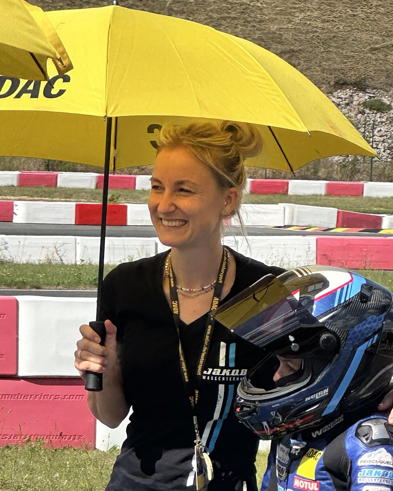 Kathi lacht unter dem ADAC-Schirm neben Valentin in der Startaufstellung