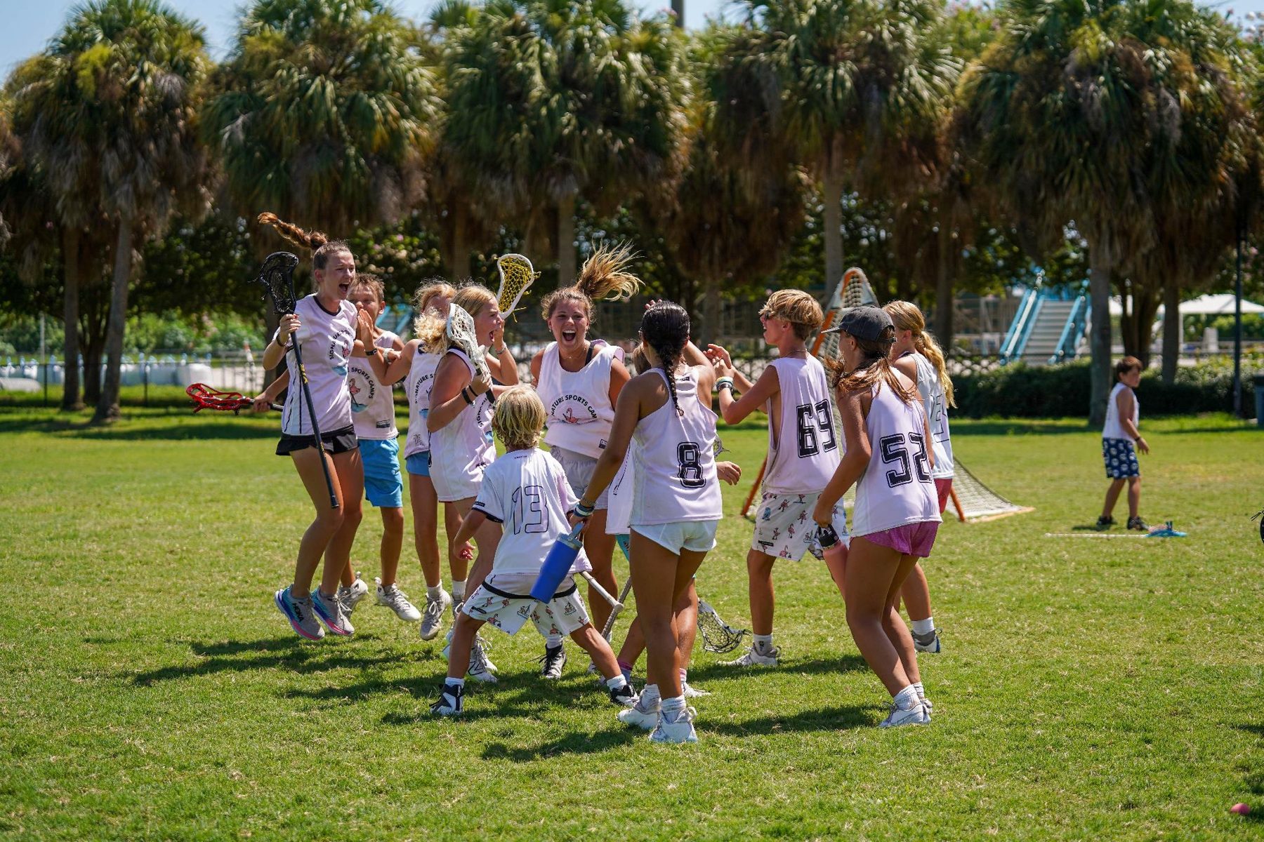 Girls lacrosse campers celebrating on a field lined with palm trees