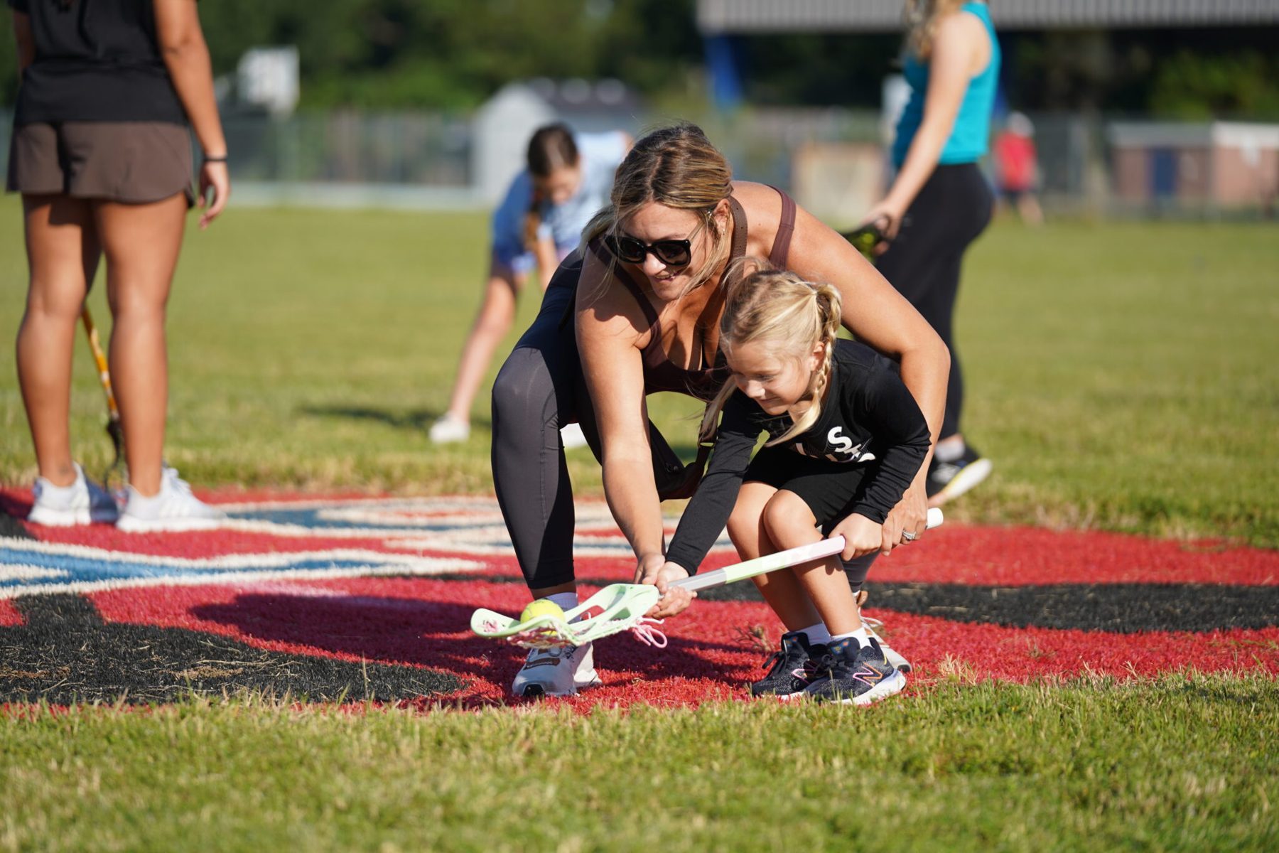 A parent helping a young child with a lacrosse stick on the field