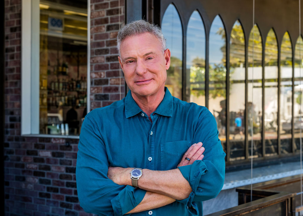 Scott Peters standing with arms crossed outside a brick storefront in San Diego