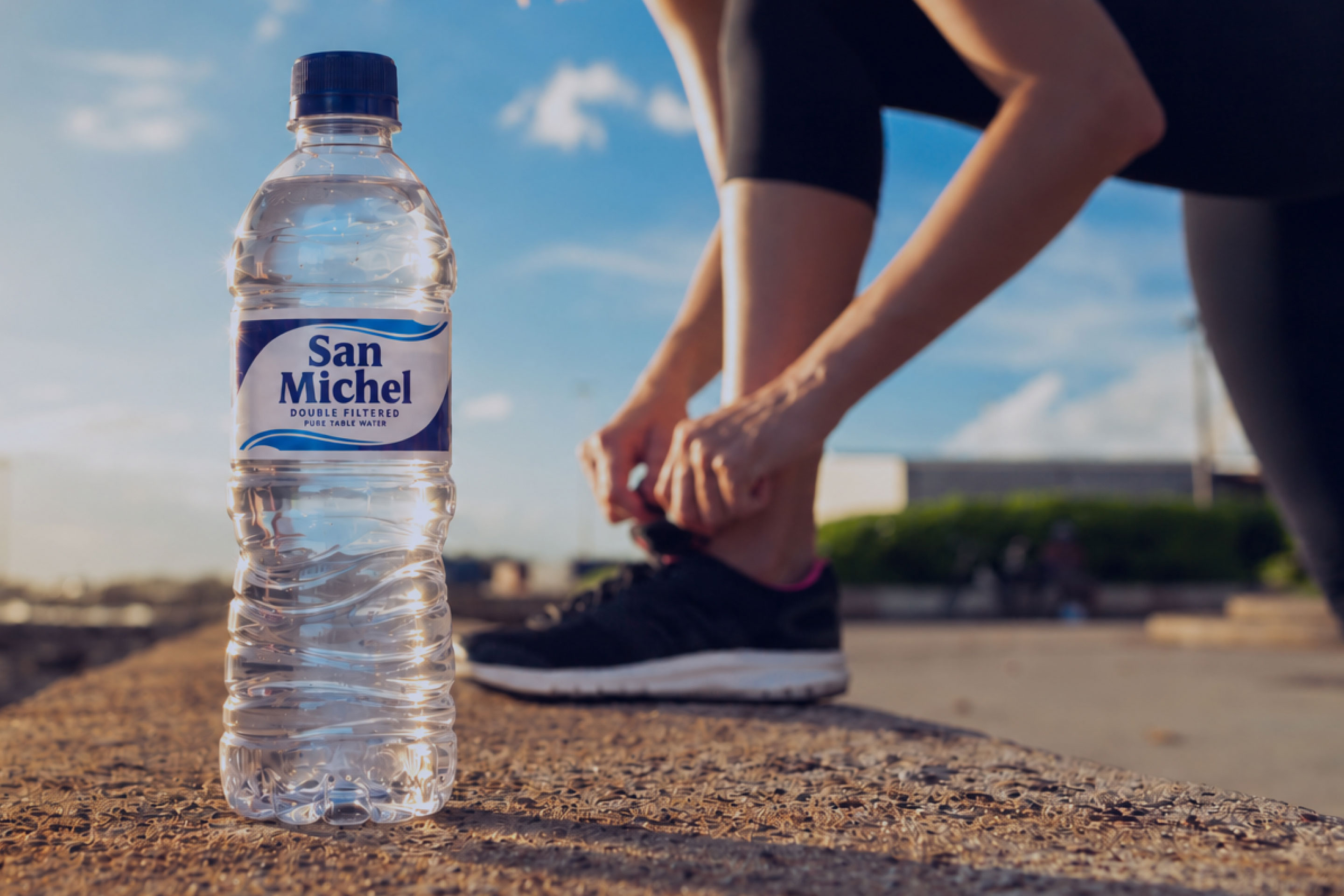 Runner tying their shoe beside a bottle of San Michel water on an outdoor track