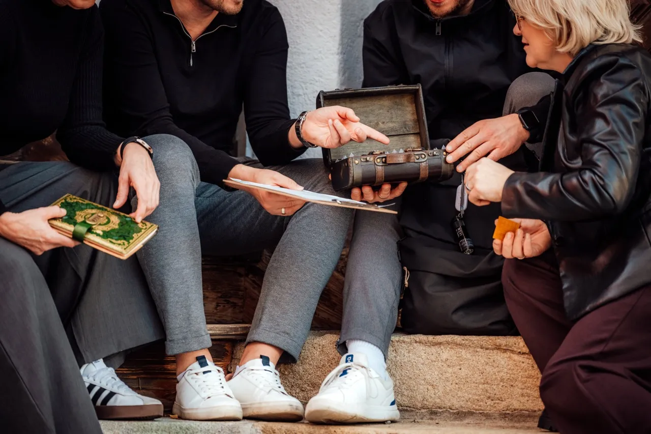 Drei Personen im herbstlichen Garten mit Koffer und Brief mit Siegel, einer zeigt lachend nach oben