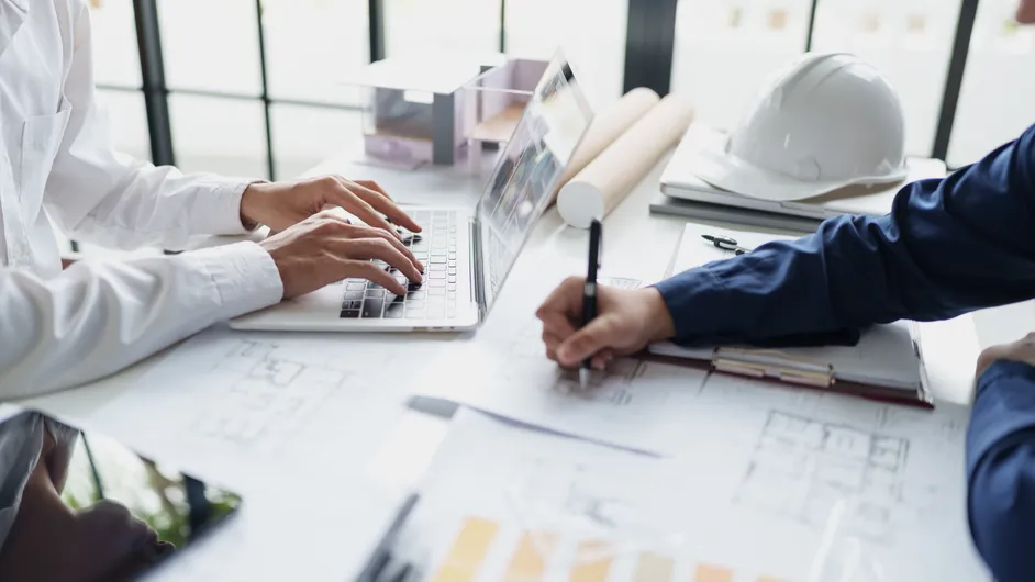 Two people reviewing plans at a desk with a hard hat.