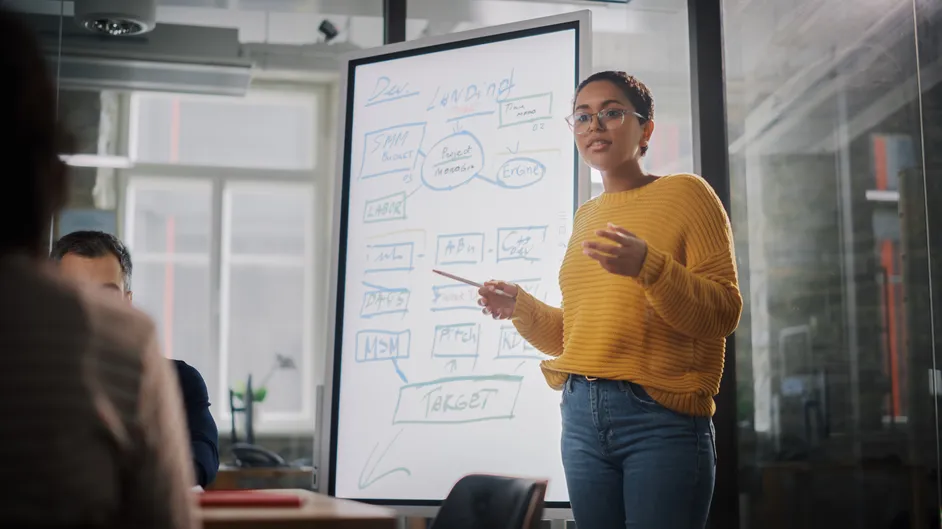 Presenter explaining a plan on a whiteboard in a meeting.