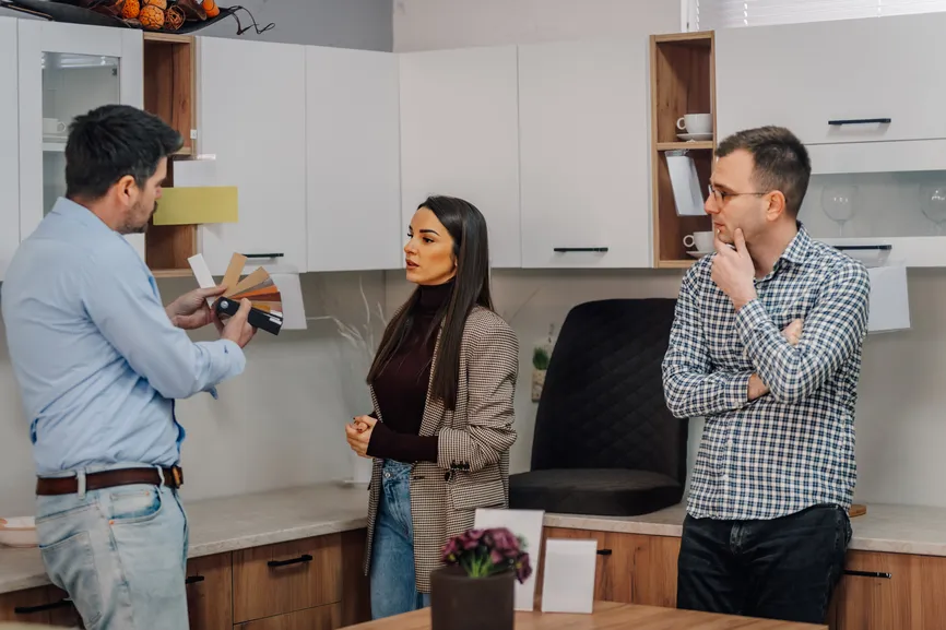 Designer showing material samples to a couple in a kitchen showroom.