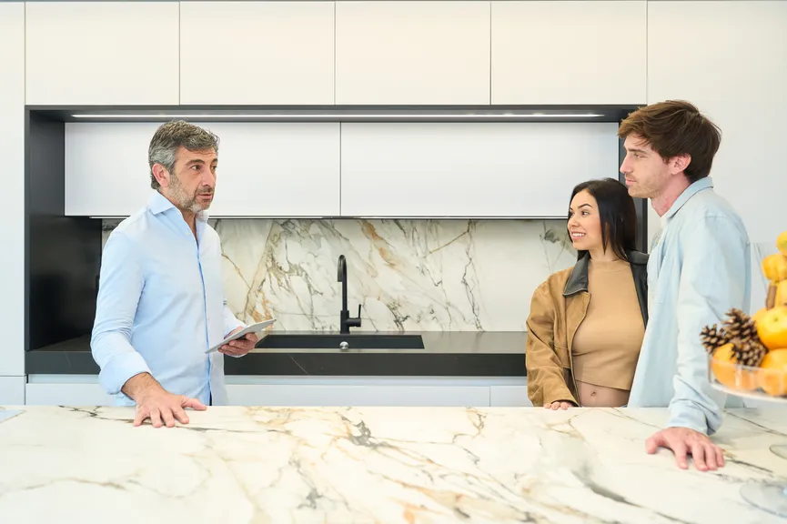 Designer reviewing plans with a couple at a marble kitchen island.