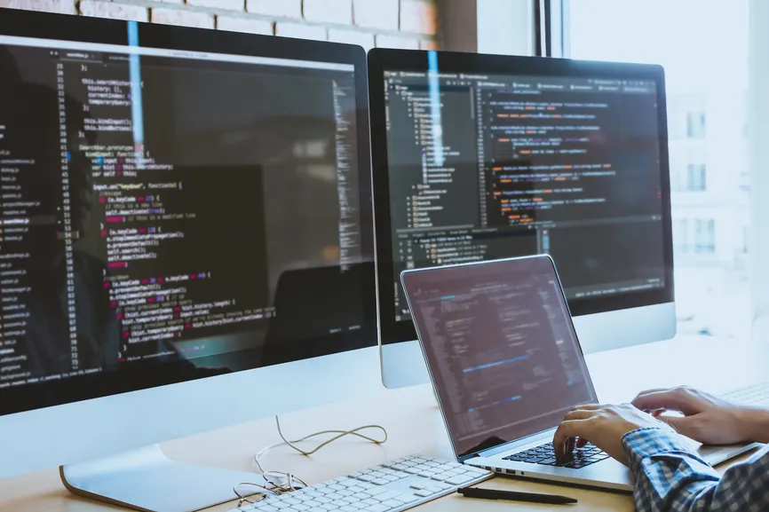 Developer on a laptop in front of two monitors of code.
