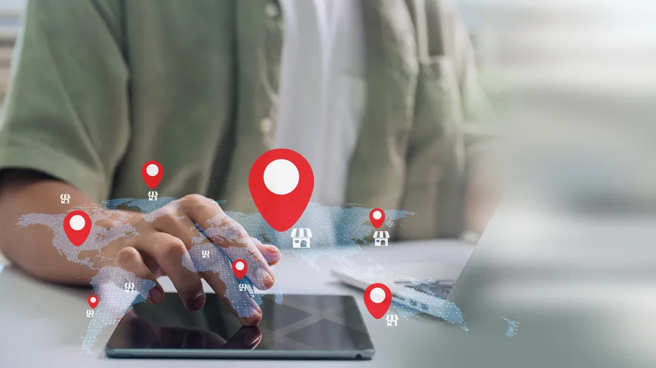 Hand on a tablet with map location pins above it.
