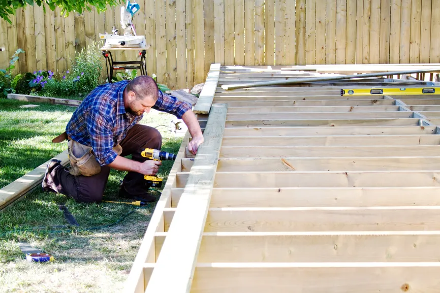 Carpenter building a wooden deck frame in a backyard.