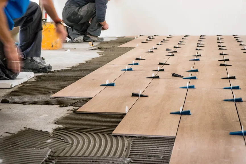 Installers laying wood-look floor tile with leveling clips.