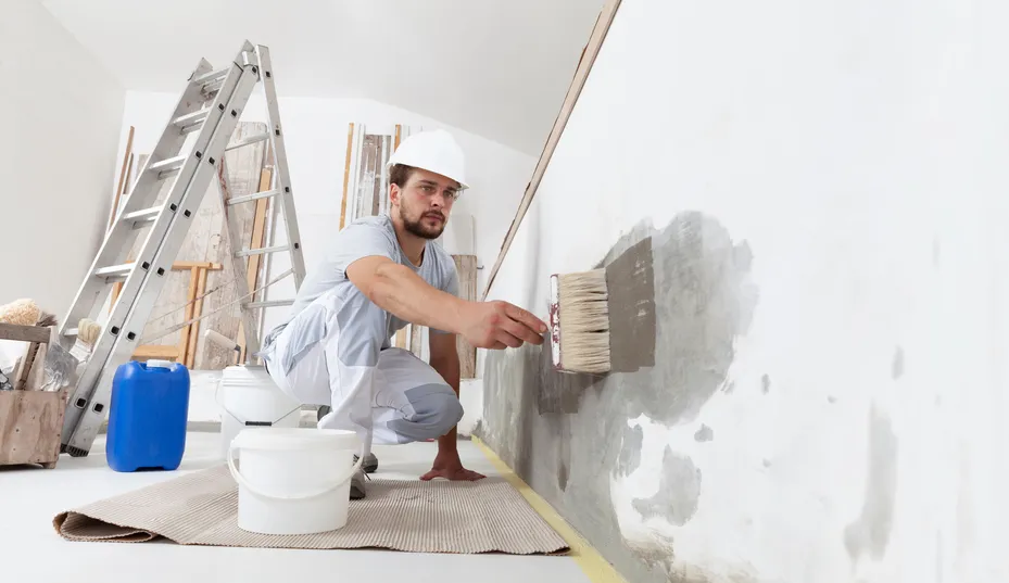 Painter in a hard hat priming an interior wall.