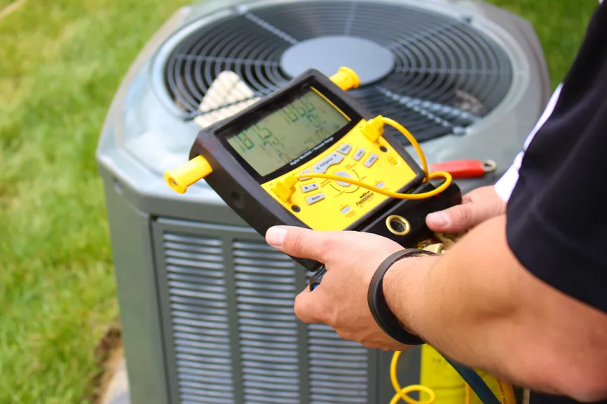 Technician holding a digital meter beside an outdoor AC condenser.