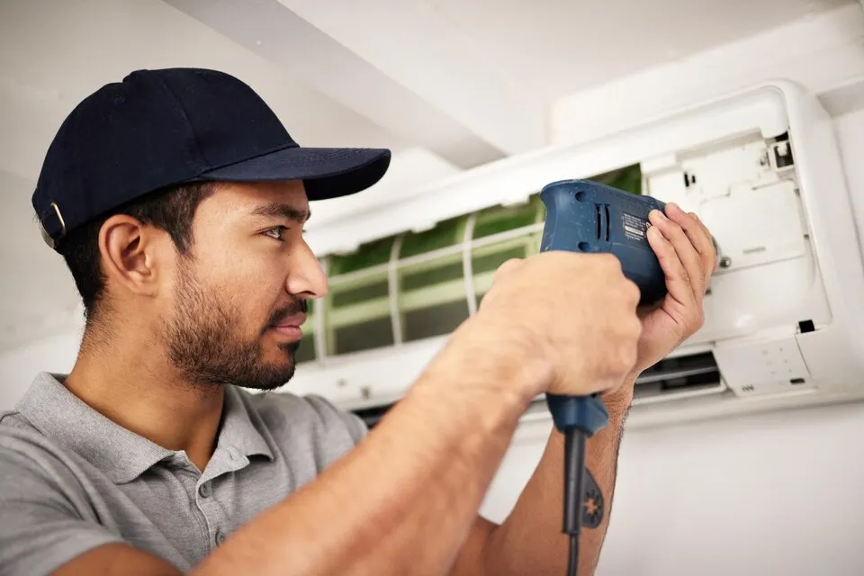 Technician repairing AC unit with drill