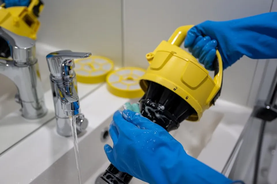 Hand in blue glove cleaning vacuum filter in sink