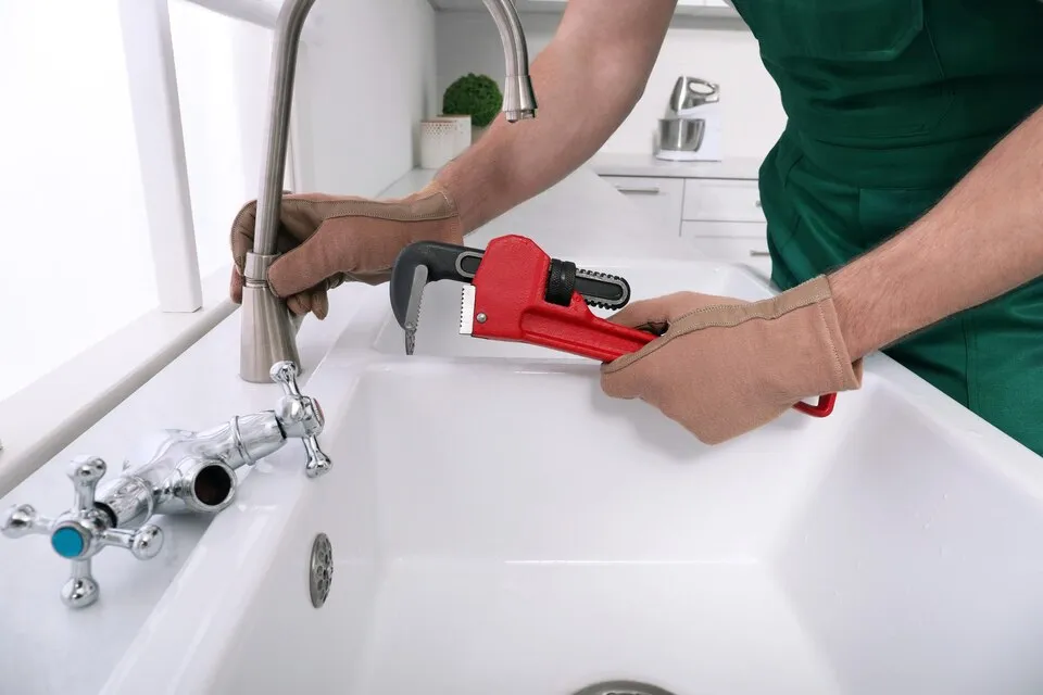 Plumber repairing a sink faucet with a pipe wrench
