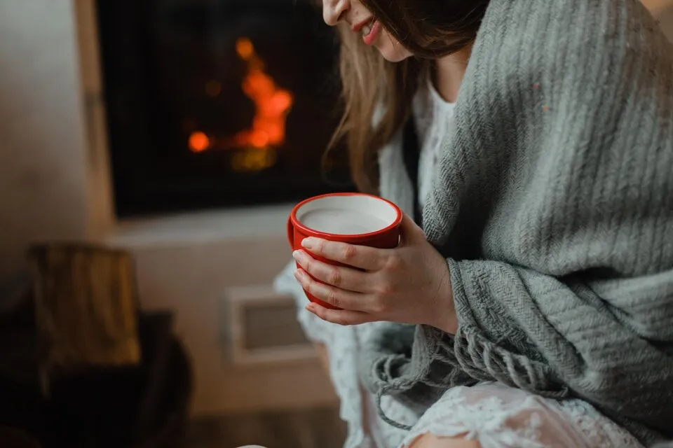 Woman enjoying a warm drink by the fireplace.