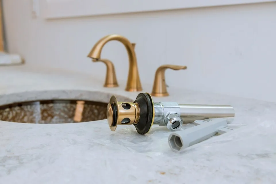 Bathroom sink drain assembly and wrench next to a faucet.