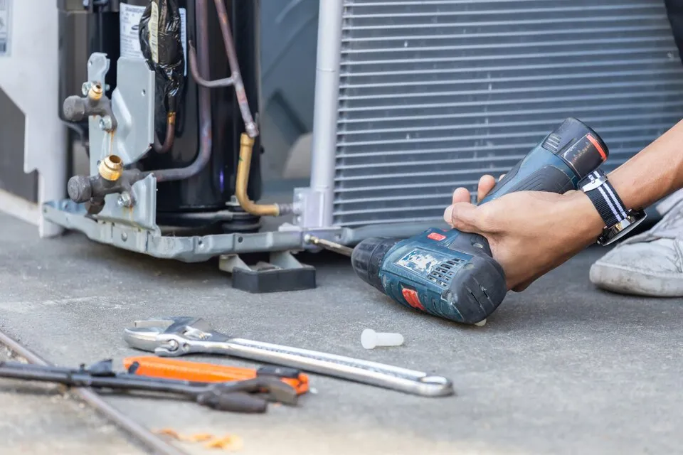 Hand holding drill near AC unit