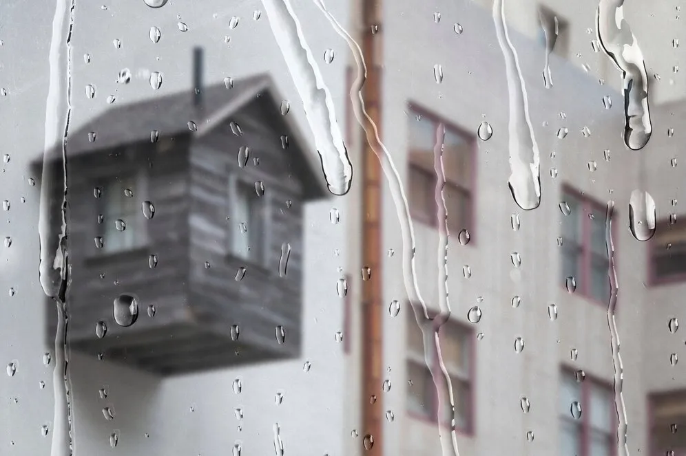 Rain drops on window, blurred house in background.