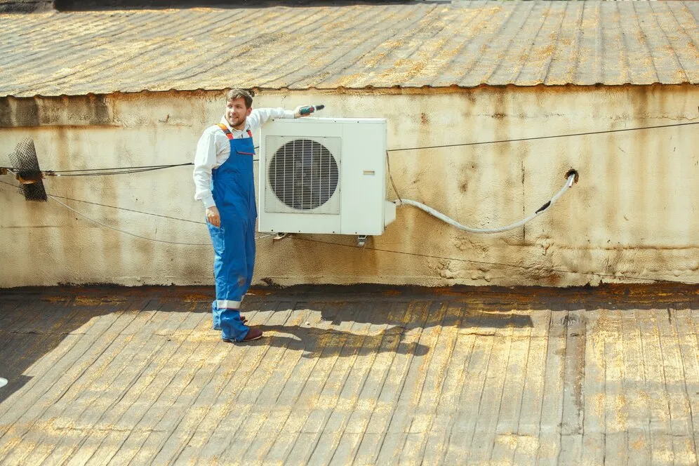 Man in overalls standing by outdoor AC unit.