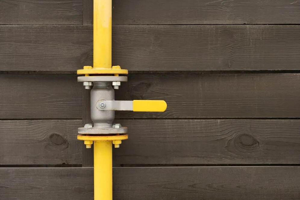Yellow gas pipe with valve on wooden wall.