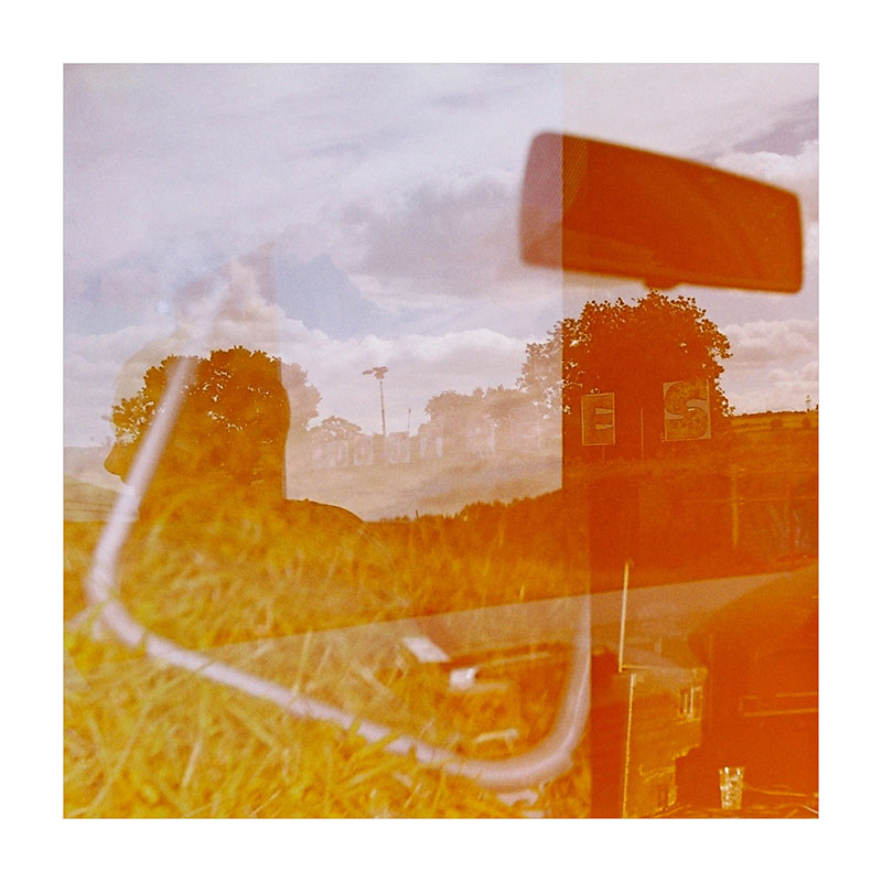 Cover art for "Singing Hearts" by Steve and the Sea. The image features a multiple-exposure photograph of various scenes from 2000 Trees music festival, such as a view from a car windscreen of the festival sign, a lawn chair on grass, and other hard to identify features. The photograph is tinged orange and yellow, and sits within a thick white border.