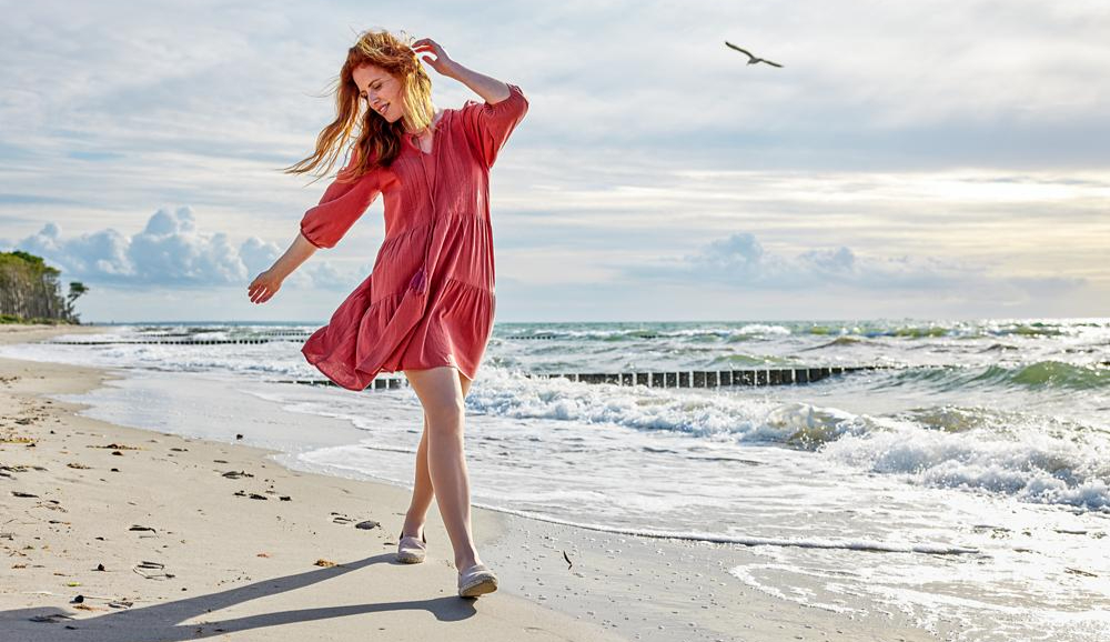 Frau im roten Kleid geht am Strand entlang