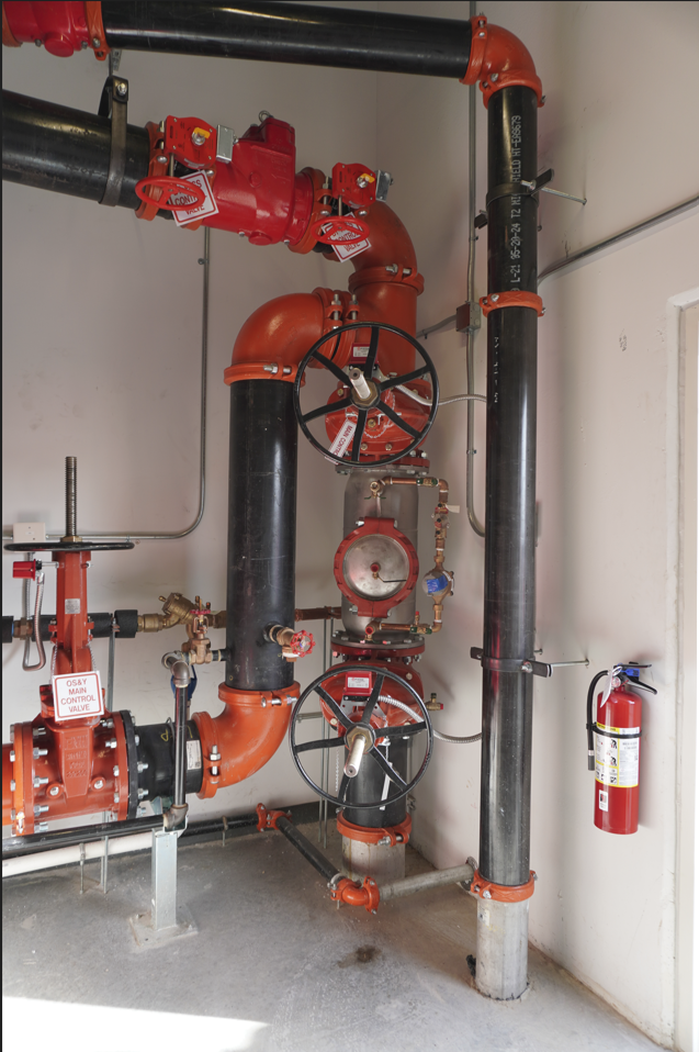 Industrial fire sprinkler system piping with valves and a red fire extinguisher mounted on the wall.