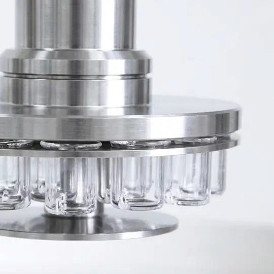 Close-up of a stainless steel machine component holding multiple small glass vials in a circular arrangement, likely part of a pharmaceutical or laboratory filling process.