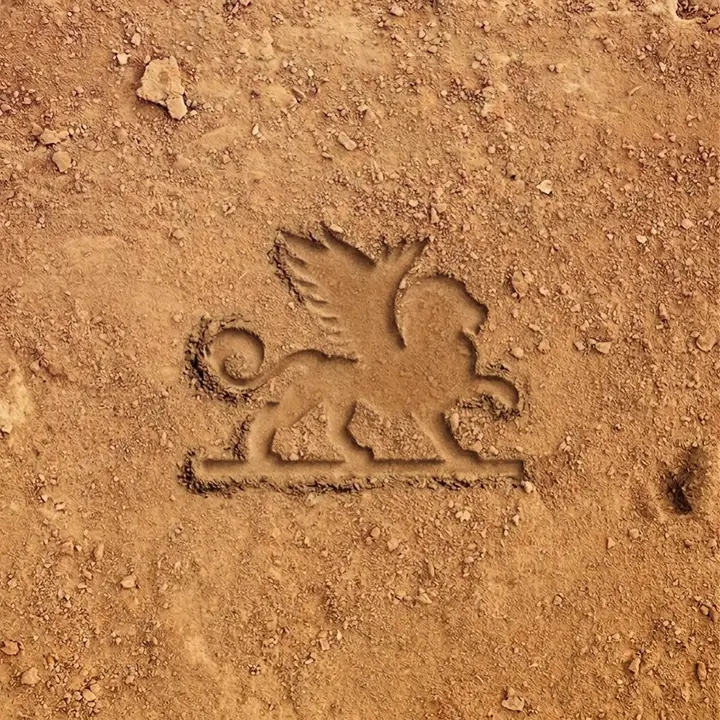Imprint of a winged lion with a curled tail and raised paw, pressed into reddish-brown dirt.