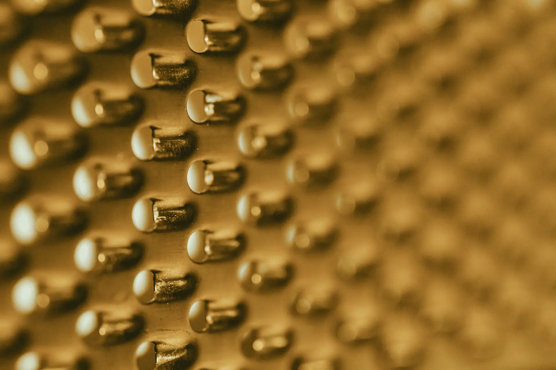 Close-up of a gold-colored metallic surface with rows of small rounded protrusions creating a textured pattern.