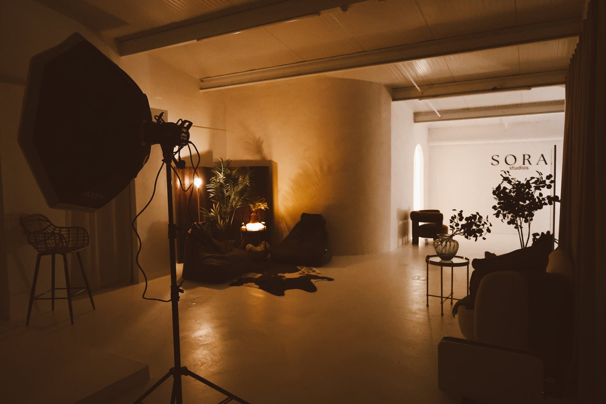 Warm-lit open studio at Sora Studios Belfast with lounge set, plants and the Sora logo wall