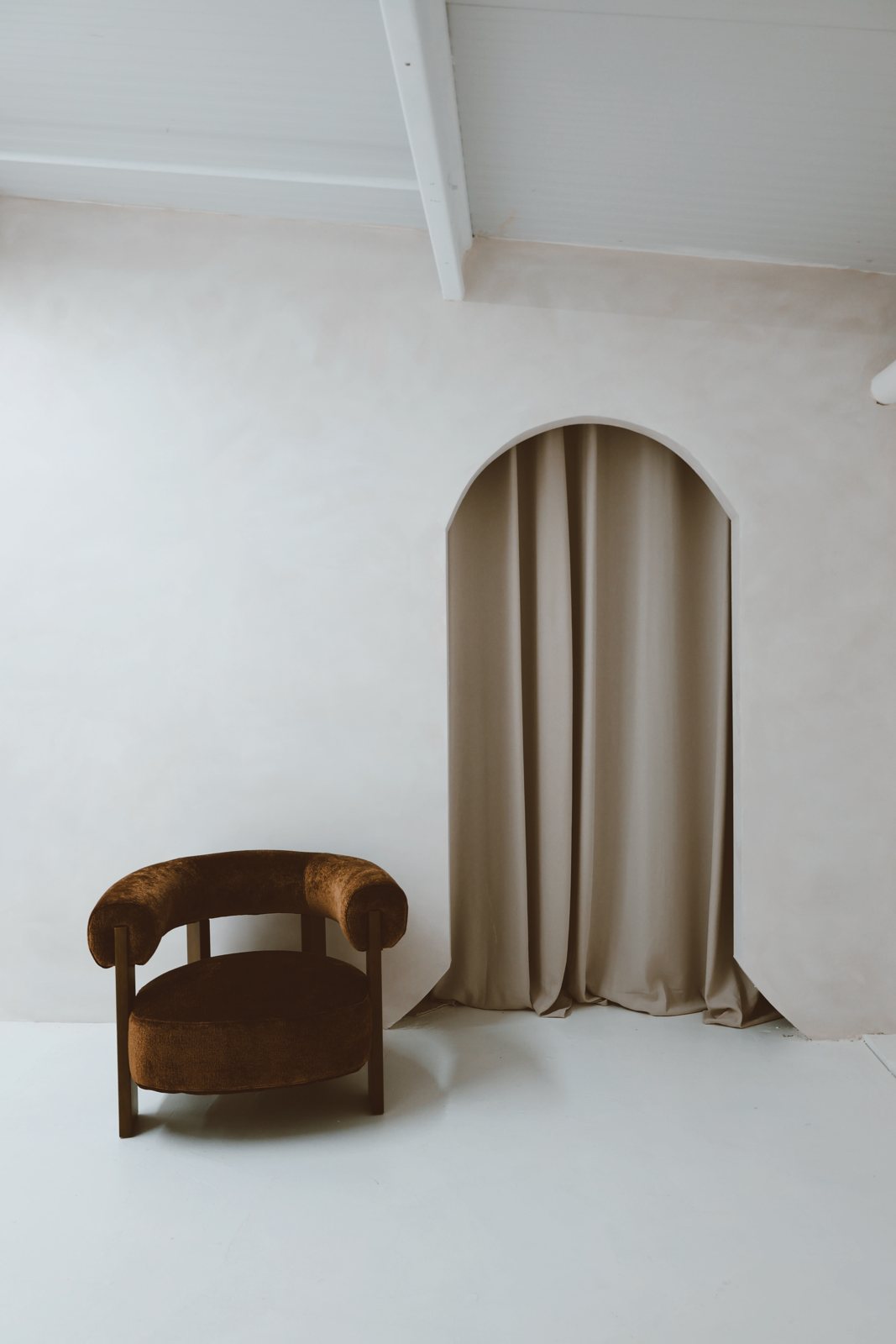 Limewash arch with draped curtain and brown bouclé armchair
