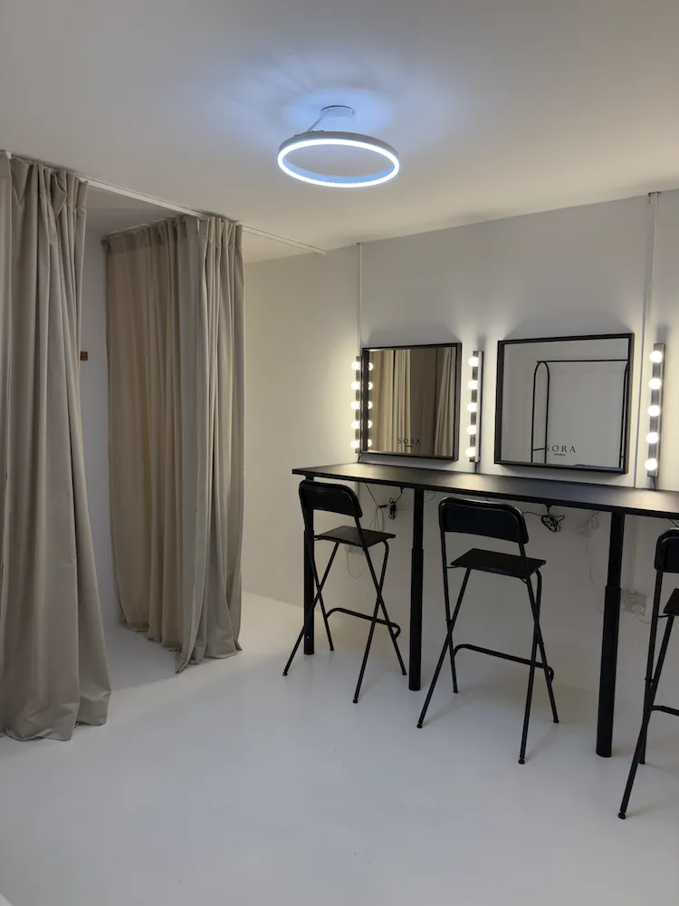 Hair and makeup stations with illuminated mirrors beside private curtained changing rooms at Sora Studios