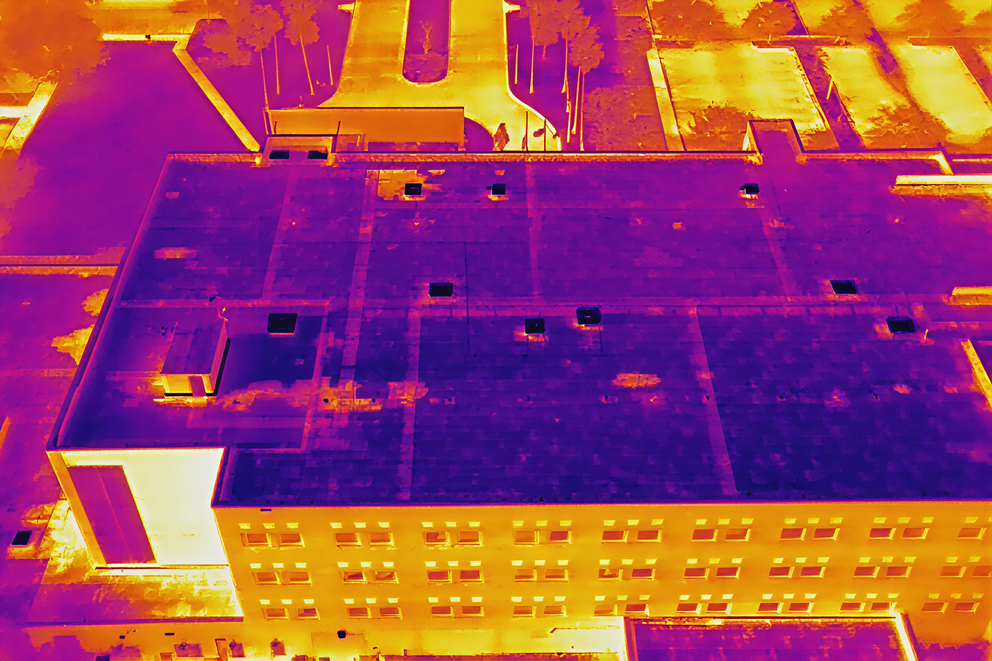 Thermal drone image of a building showing roof and adjacent areas with heat variations in purple, orange, and yellow tones.