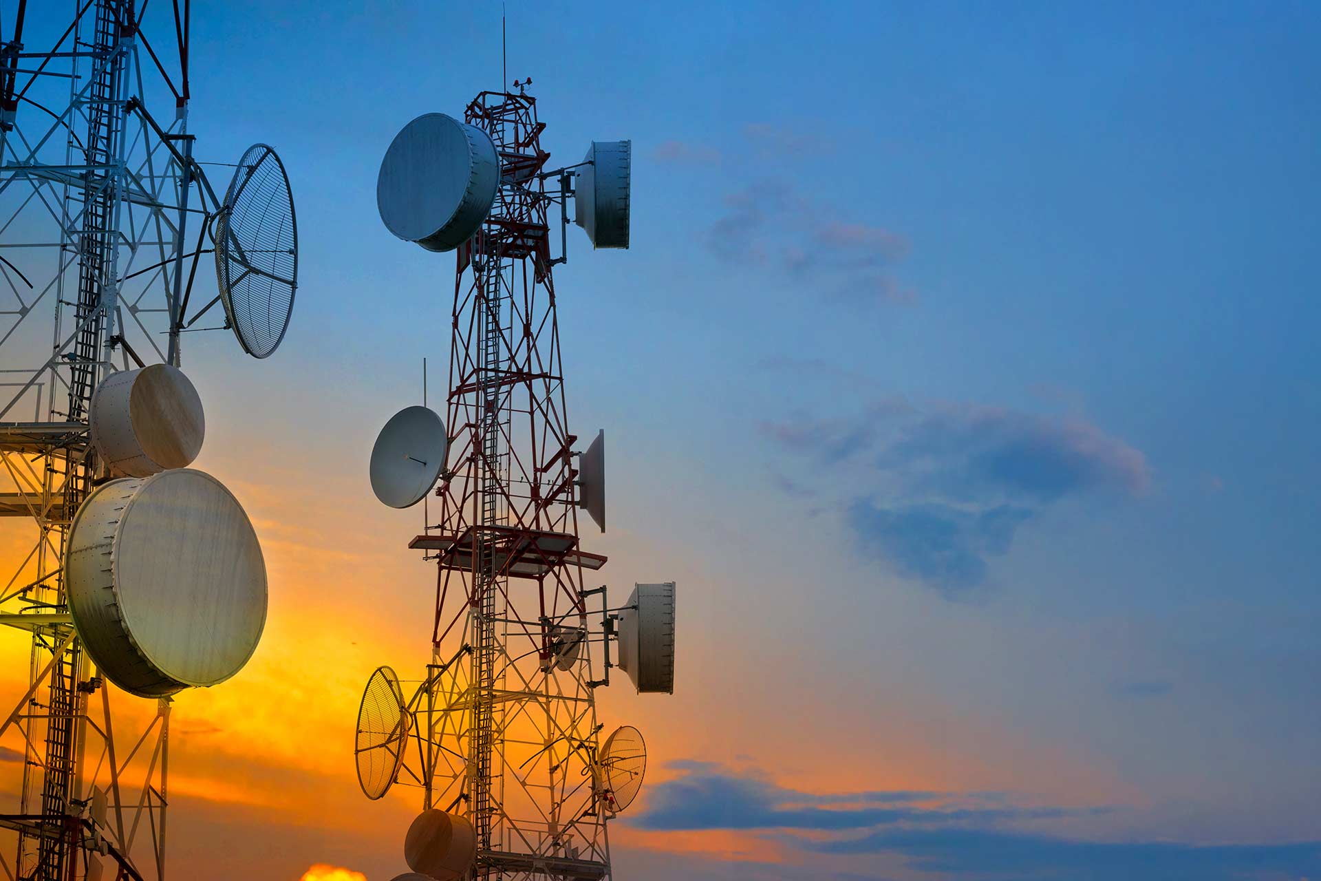 Cell towers with microwave dishes and antennas against a sunset sky