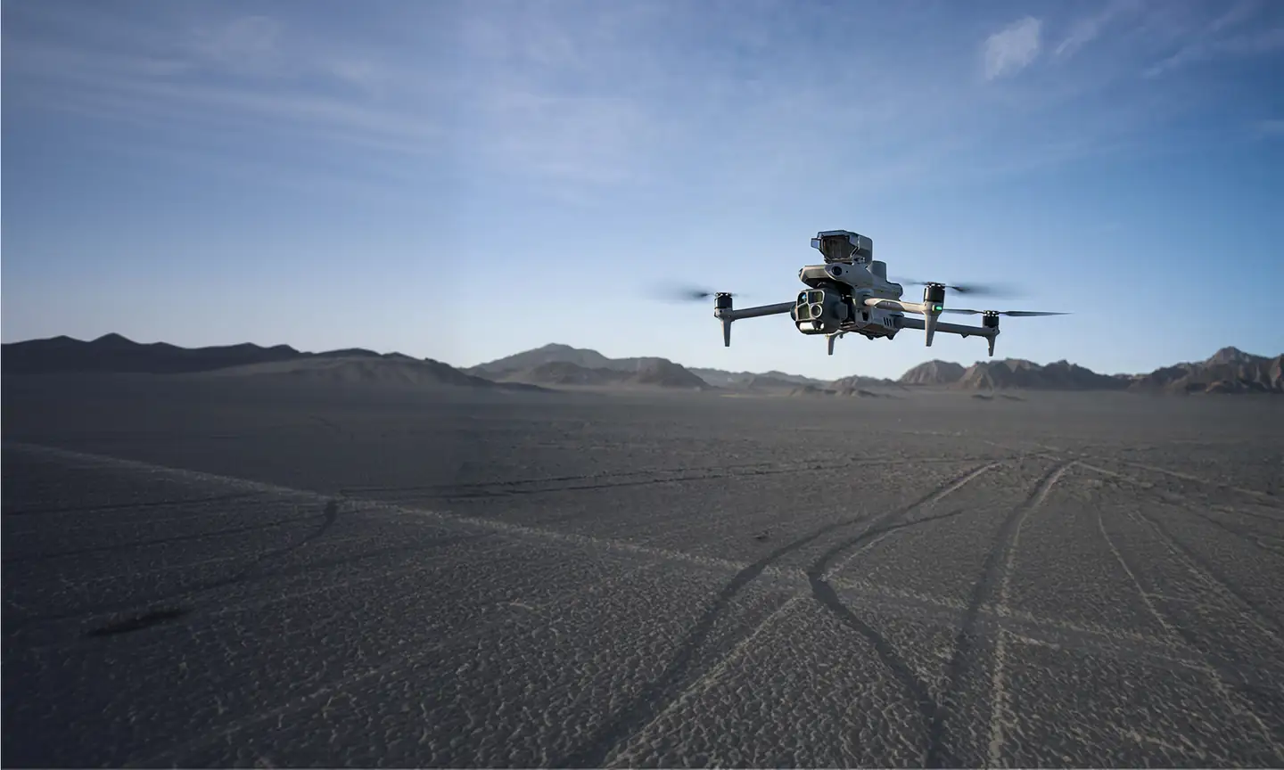 Commercial drone hovering low over a wide desert landscape under a blue sky