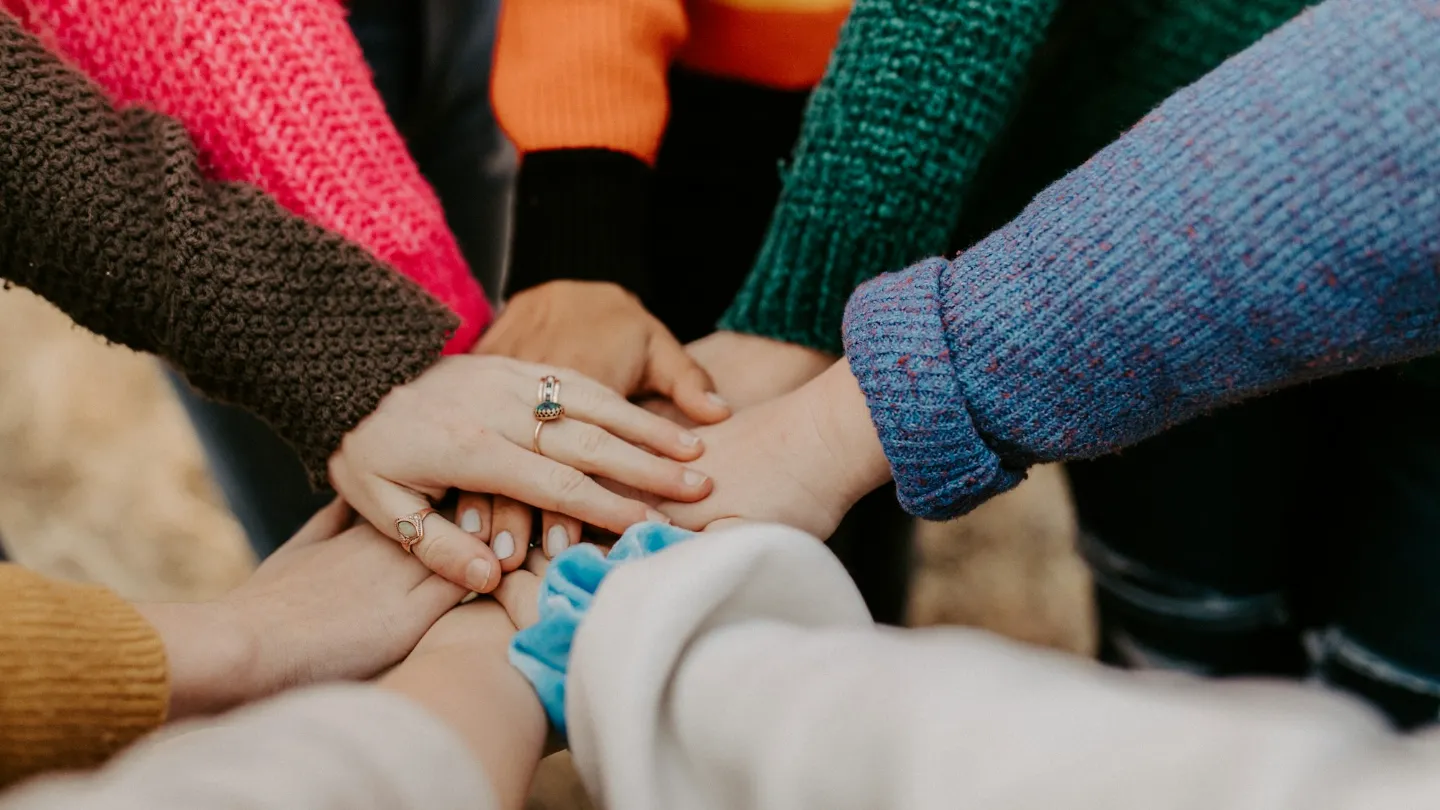 Several people's hands stacked together, in colorful sweaters