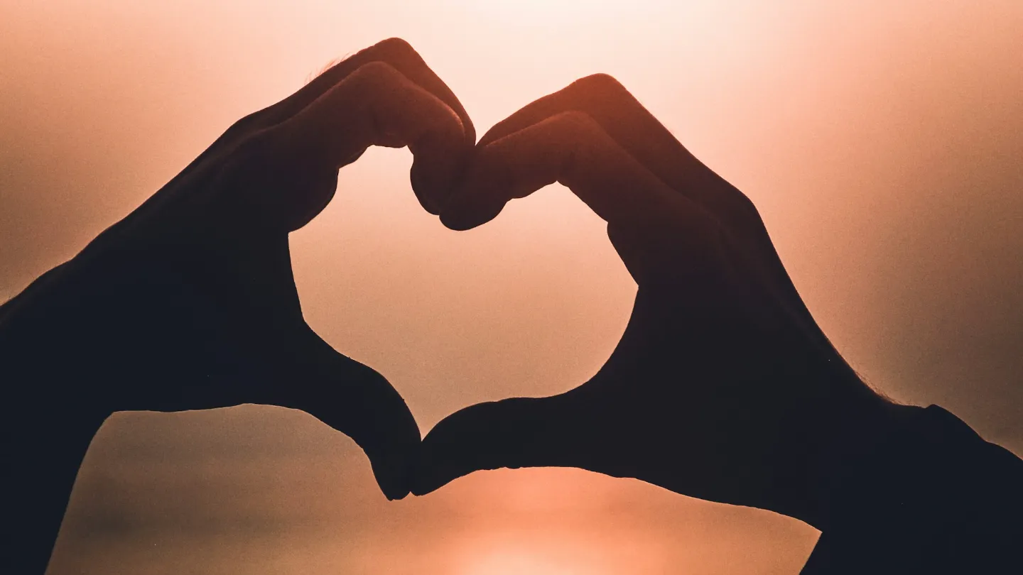 Two hands making a heart shape against a sunset