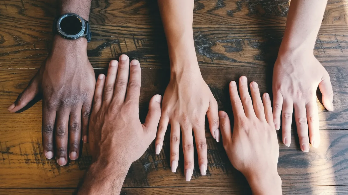 Five hands resting side by side on a wooden table