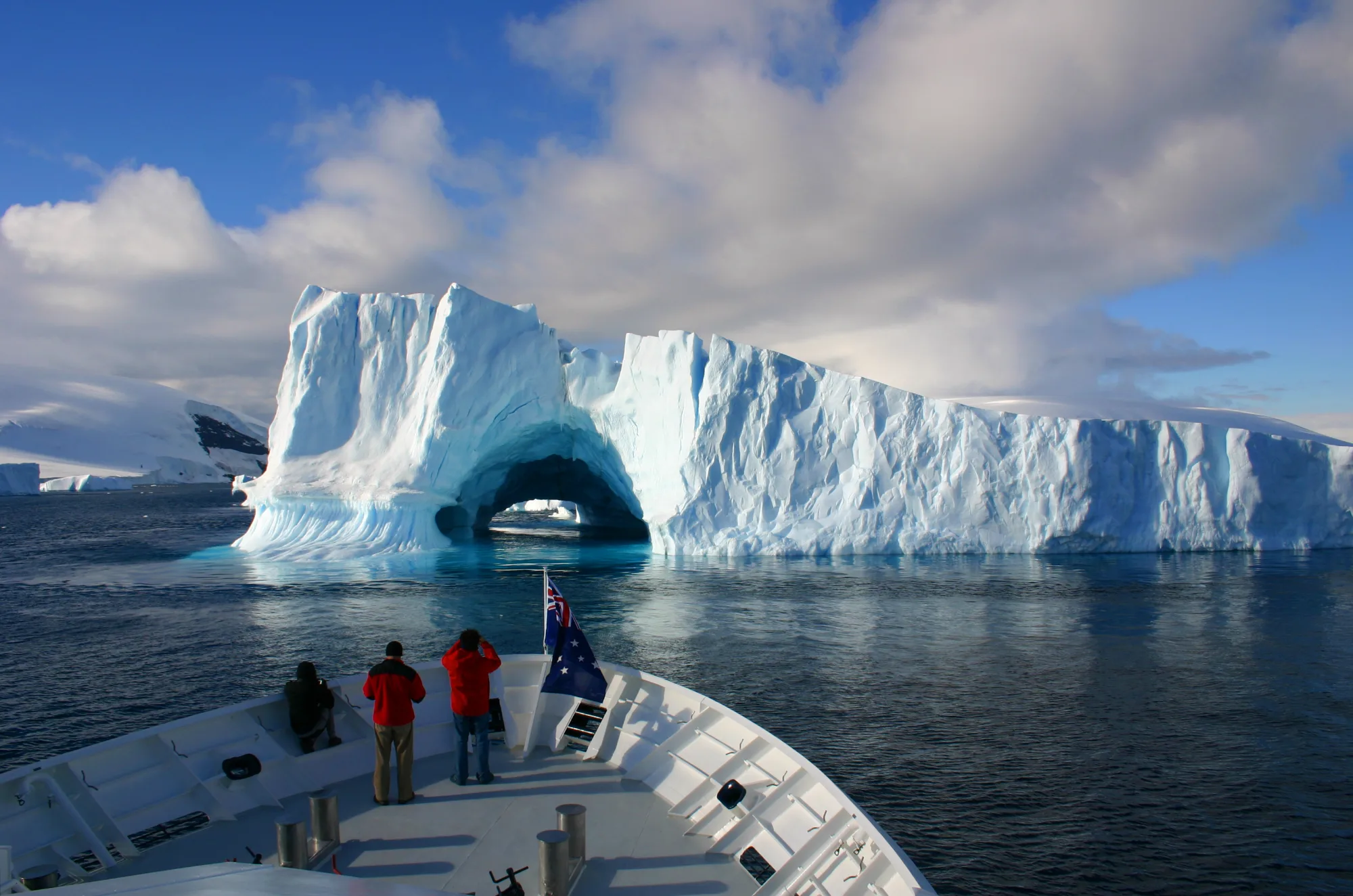 Guests at the bow of an expedition ship watching an Antarctic ice arch