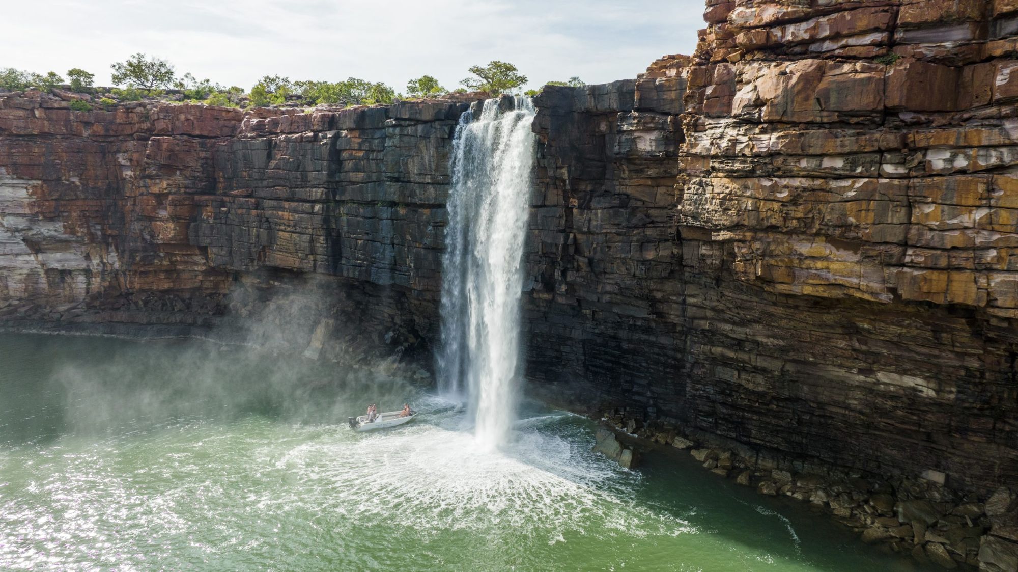 Tender beside a waterfall plunging over layered red cliffs in the Kimberley