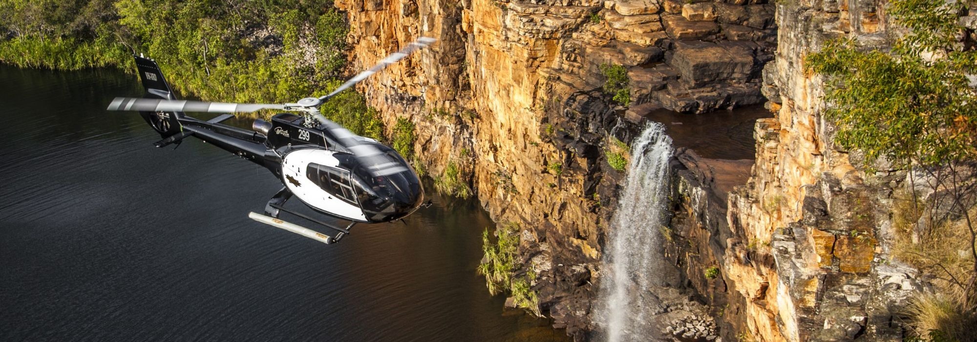 Helicopter flying past a waterfall and sandstone cliffs in the Kimberley