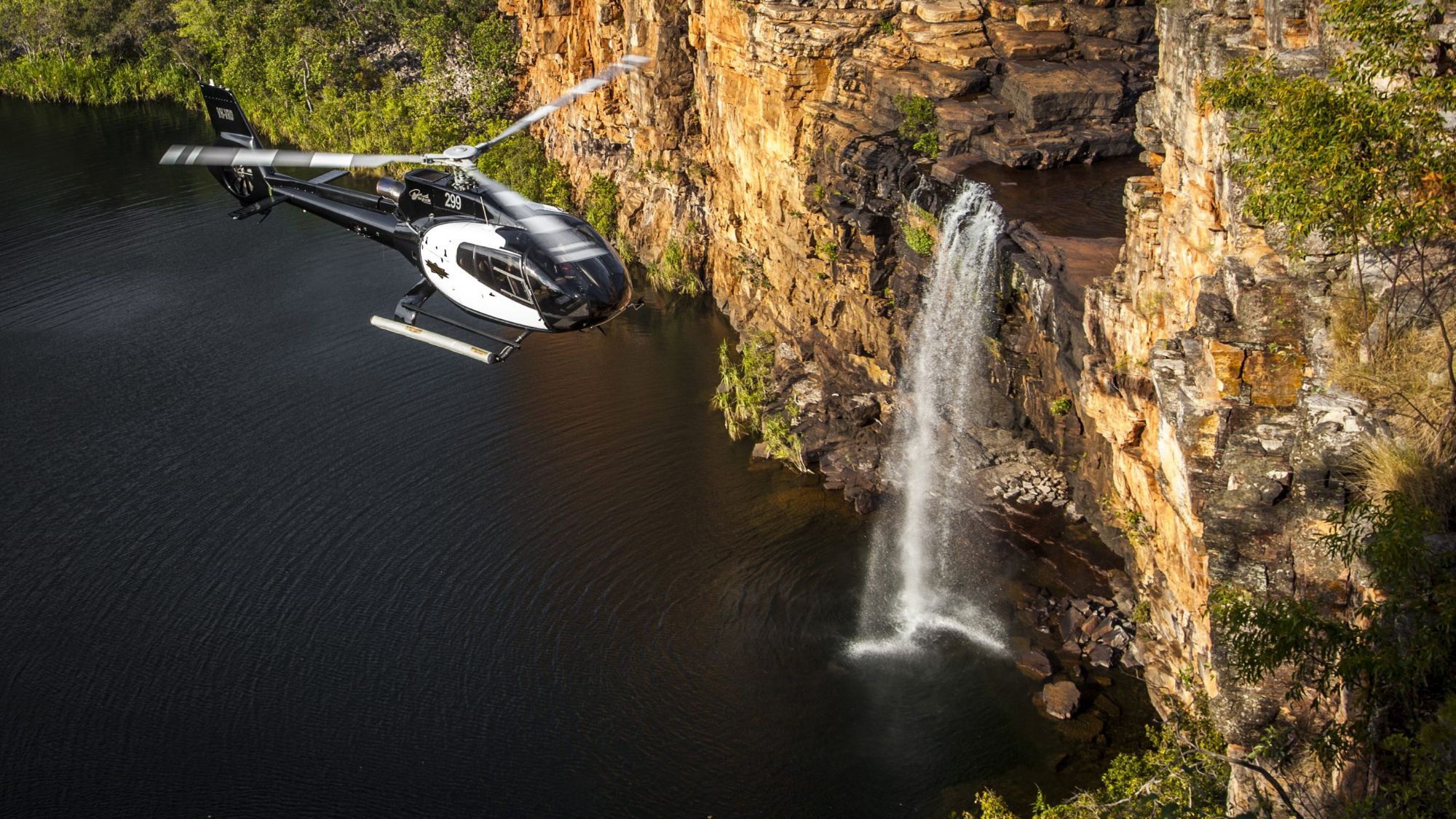 Helicopter flying past a waterfall and sandstone cliffs in the Kimberley