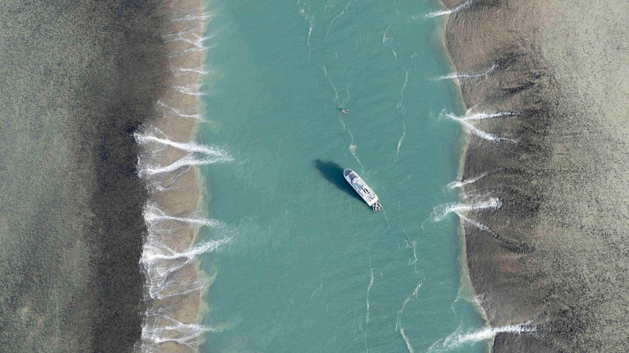 Aerial view of an expedition ship anchored in a turquoise tidal channel